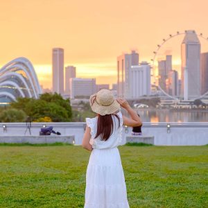 Young Woman traveling with hat at Sunset, happy Asian traveler visit in Singapore city downtown. landmark and popular for tourist attractions. Asia Travel concept