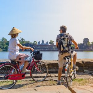 Tourist couple cycling in Angkor temple, Cambodia. Angkor Wat main facade reflected on water pond. Eco friendly tourism traveling.